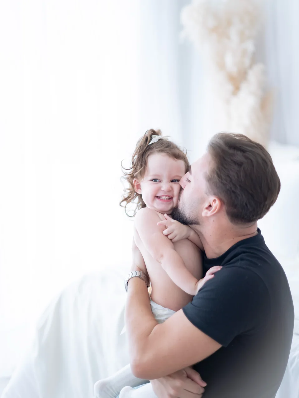 Samuel segurando a filha no colo e beijando seu rosto enquanto ela sorri
